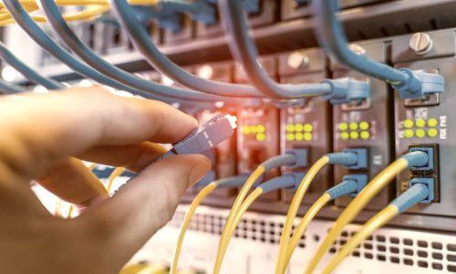 hand with fiber network cables connected to servers in a datacenter